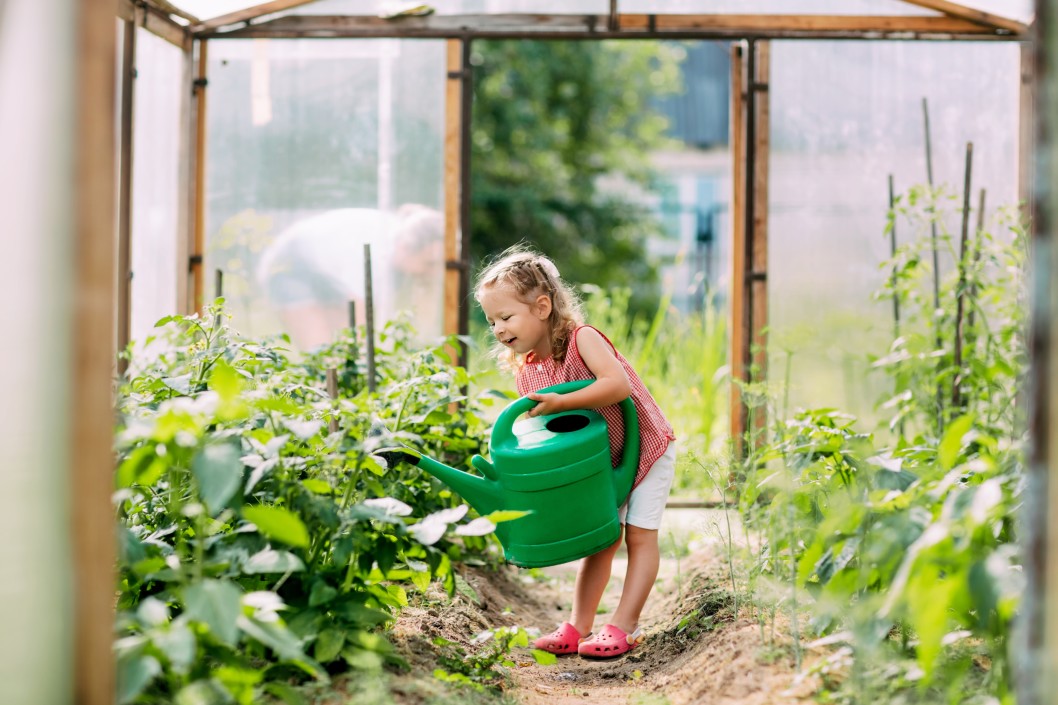 Mädchen gießt Pflanzen im Gewächshaus